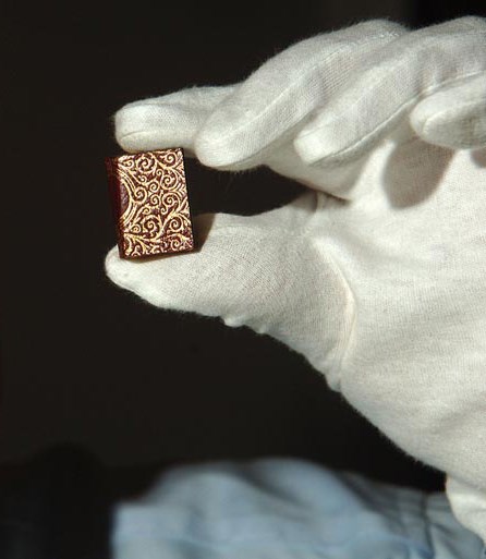 A white gloved hand holding a miniature Qur'an.