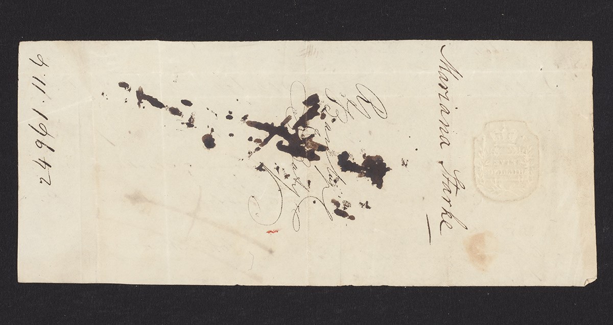 A piece of old yellowed paper with the name "Mariana Starke" written on it in ink. There are ink stains covering other writing on the page.