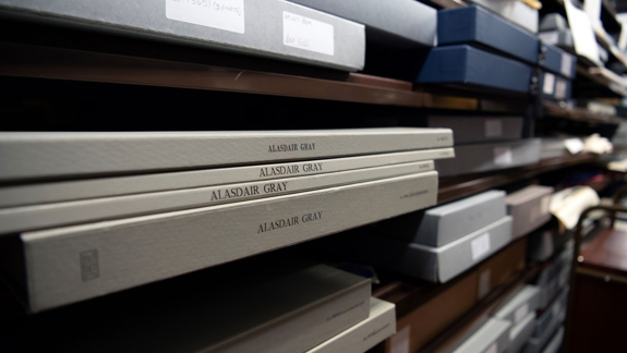 Boxes on shelves full of Alasdair Gray material.