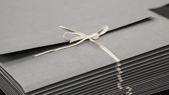 Someone tying thin grey folder closed with cotton tape.