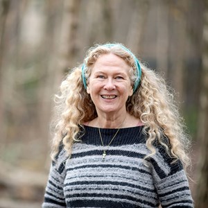 A photo of a women with long, curly, blonde hair. She is wearing a teal headband, a fuzzy black and white jersey and a necklace.