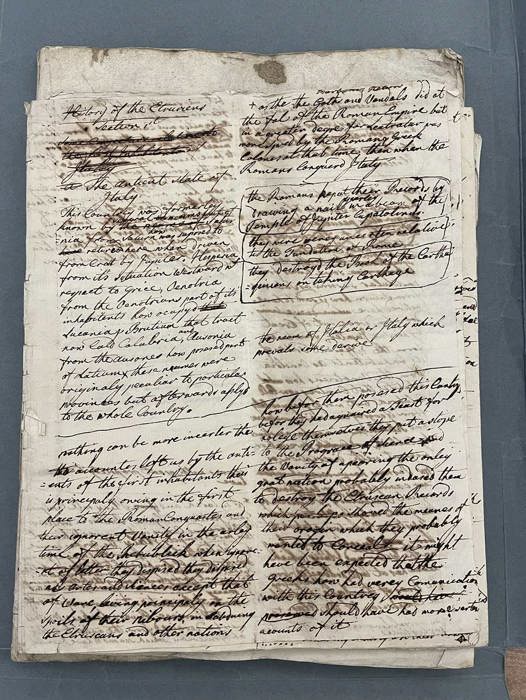 Two handwritten manuscript pages filled with dense ink notes and heavy crossings‑out, laid open on a table.