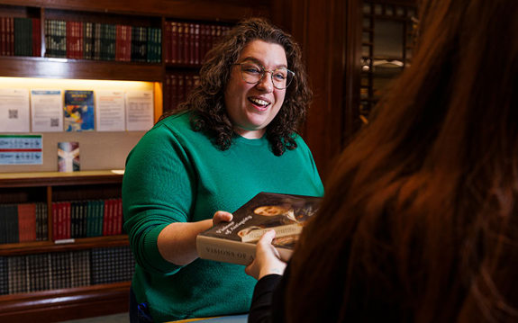 A smiling librarian handing a reader a book over a desk