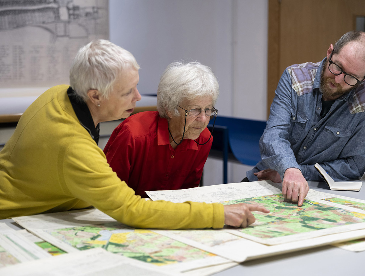 Three adults standing around a table pointing at a map.