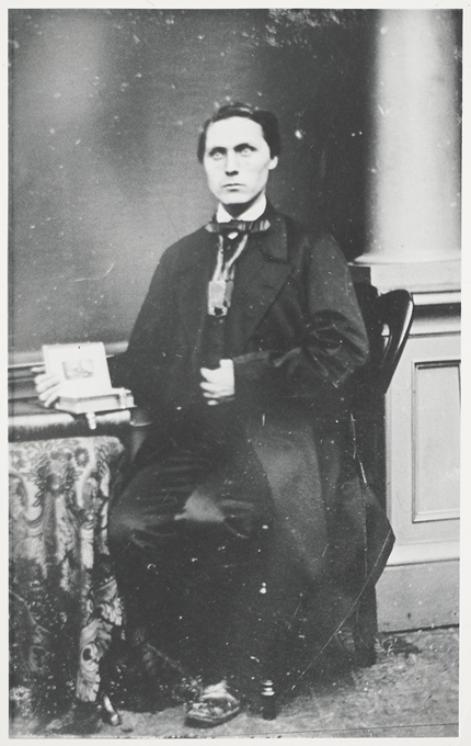 A black and white photo of a man sitting holding an open book.