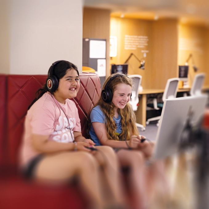 Two children sitting on a bench listening to something in Kelvin Hall.
