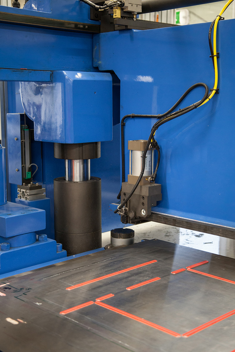 A blue machine with wires. On the base is a pattern marked out in red.