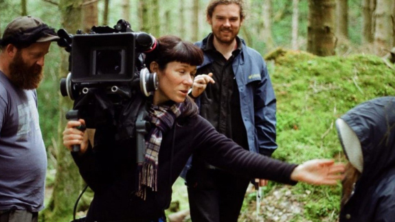 A female director holds a camera and directs a young actress.