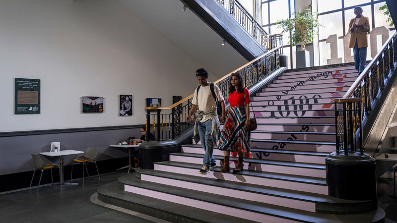 People walking down the main staircase in the George IV Bridge building which shows centenary branding.