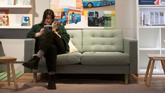 An adult sits on a couch reading a book.