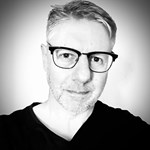 Black and white headshot of a man with glasses on.