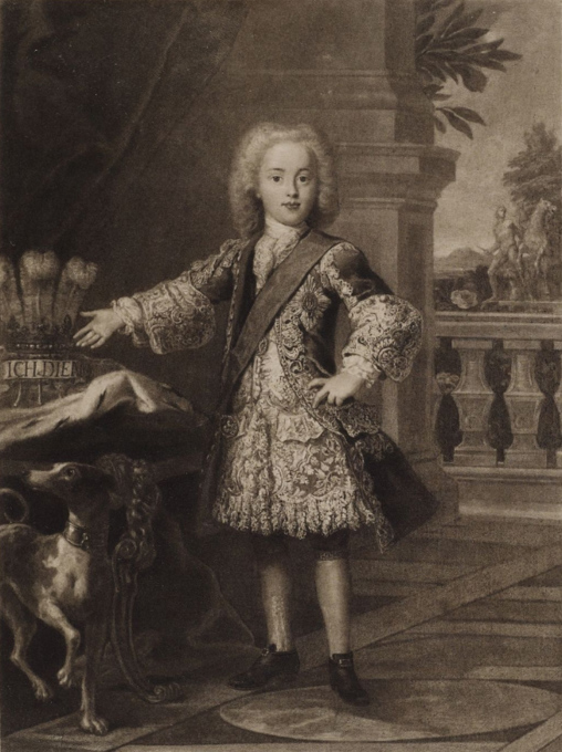 Portrait of Prince Charles as young boy, standing in room with very ornate jacket on, next to a table, with a dog underneath table.