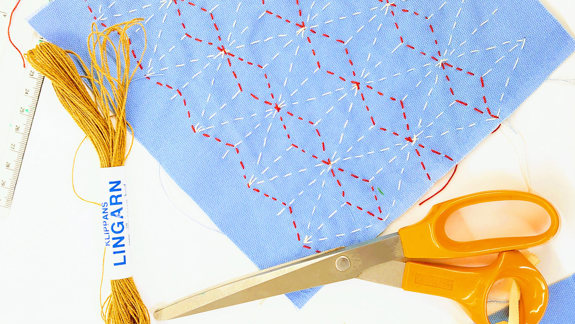 A square of fabric with patterned stitching, thread, and a pair of scissors.
