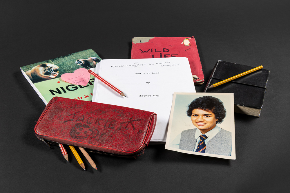 Ephemera from Jackie Kay's archive including a pencil case, notebooks, and a school photo.