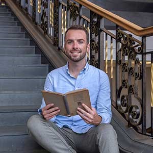 2023 Scots Scriever Shane Strachan sitting on the stairs of the National Library at George IV bridge holding a book.