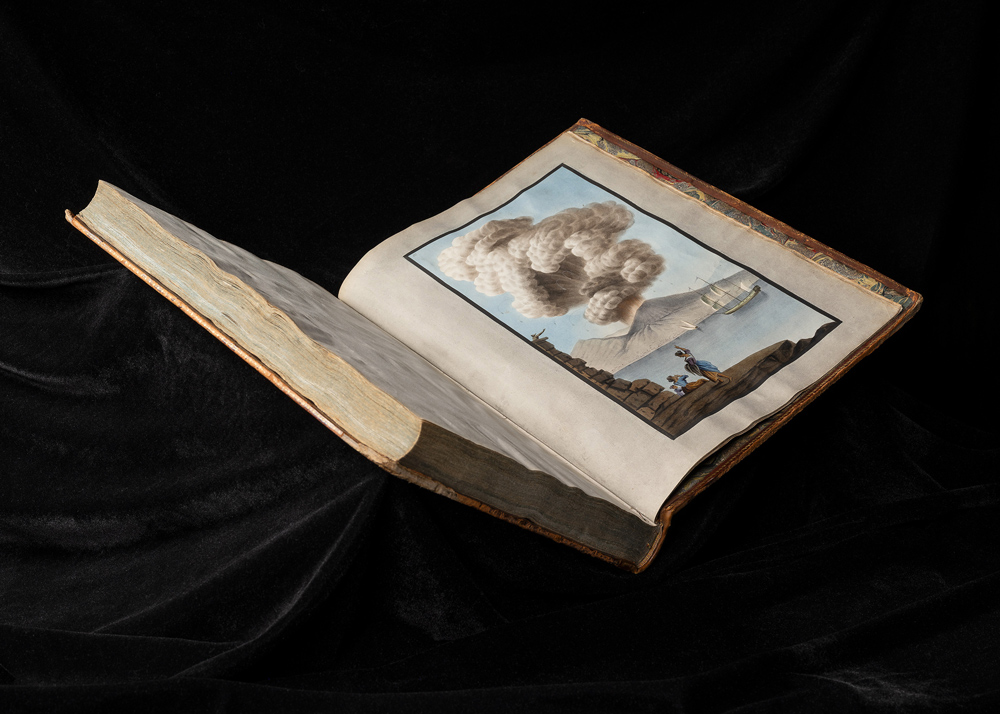 An open book showing an illustration of an erupting volcano on the coast with people looking on.