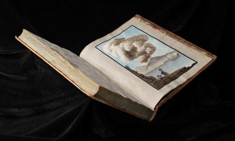 An open book showing an illustration of an erupting volcano on the coast with people looking on.