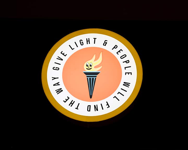 A flame framed by a circle with the words 'Give light and people will find the way'