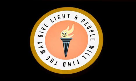 A flame framed by a circle with the words 'Give light and people will find the way'