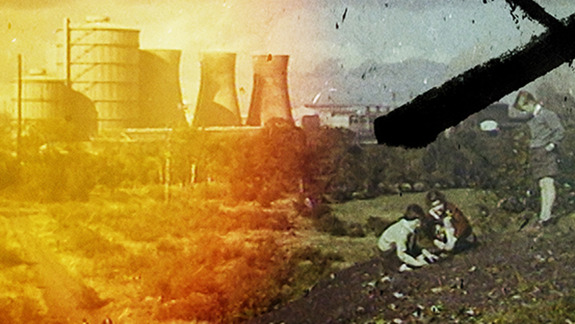 A film still showing a power plant on one side and children playing on a hill on the other.