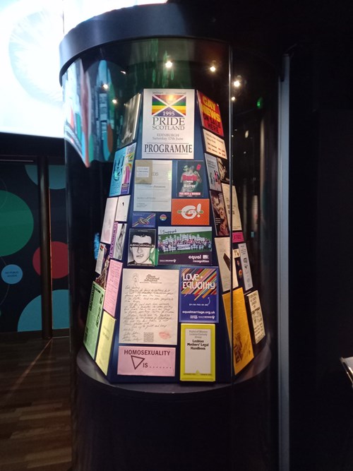 A circular exhibition case full of LGTQT+ archival material and ephemera.