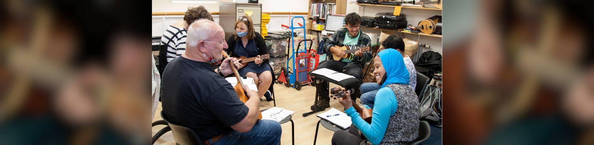 A group of people sitting in a circle playing ukeleles.