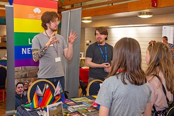 Two people standing at a stall talking to two members of the public.