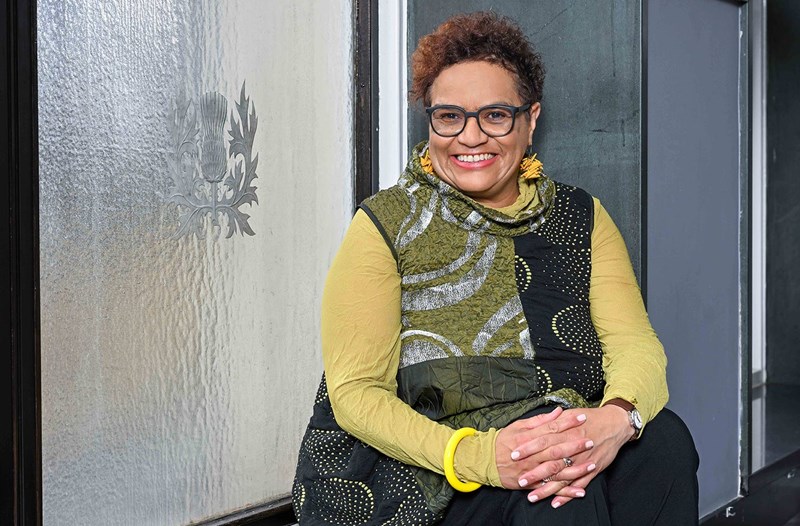 A woman sits against a thistle window smiling.