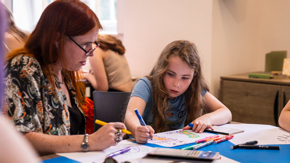 An adult and a child siting at a table drawing pictures.