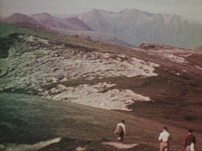 An old coloured film still of three men climbing a mountain.