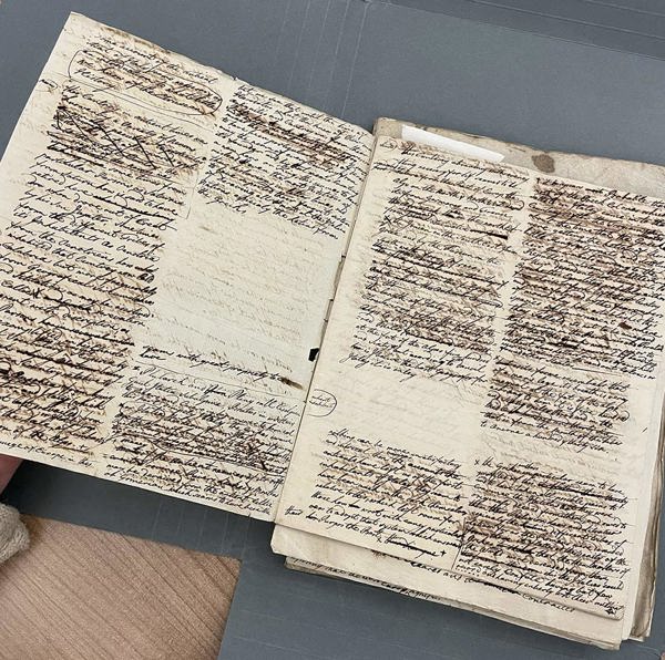 Two handwritten manuscript pages filled with dense ink notes and heavy crossings‑out, laid open on a table.