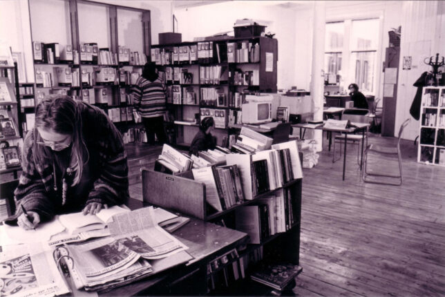 A black and white photo of Glasgow Women's Library with shelves full of books and someone writing something down.