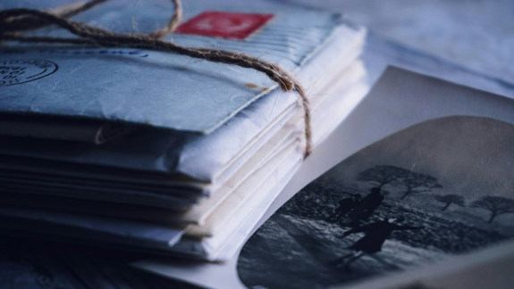Colour photo of a close-up of some twine-bound letters and out of focus vintage photographs.