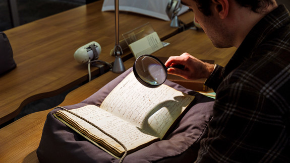 A person looking at a manuscript with a magnifying glass.