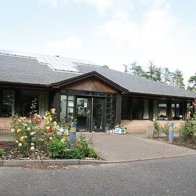 A photograph of the front Milestone house with a driveway and roses in the front.