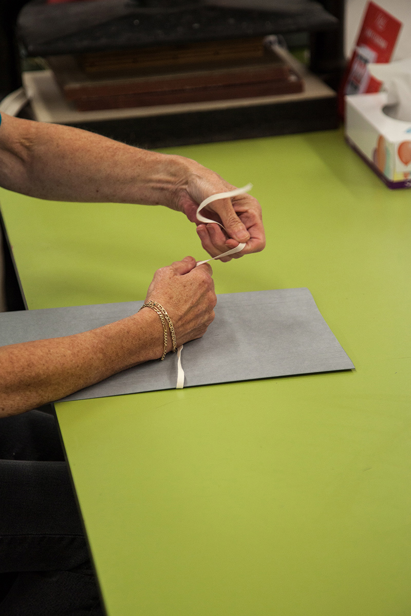 Someone tying thin grey folder closed with cotton tape.