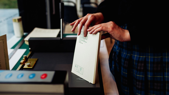 A person holding a book titled 'Making Public Press' standing next to a machine.