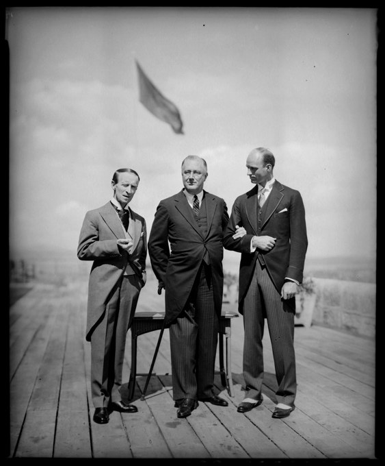 Three men stand together with a flag in the background