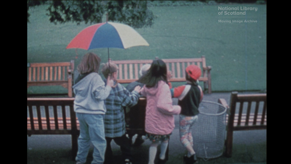 One child holding an umbrella alongside three other children in a park.