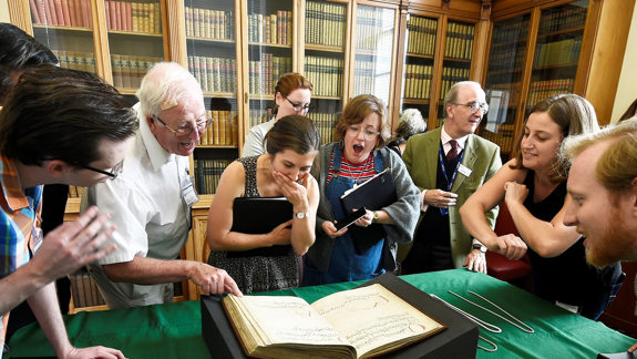 Several people standing around a table looking at an old manuscript.