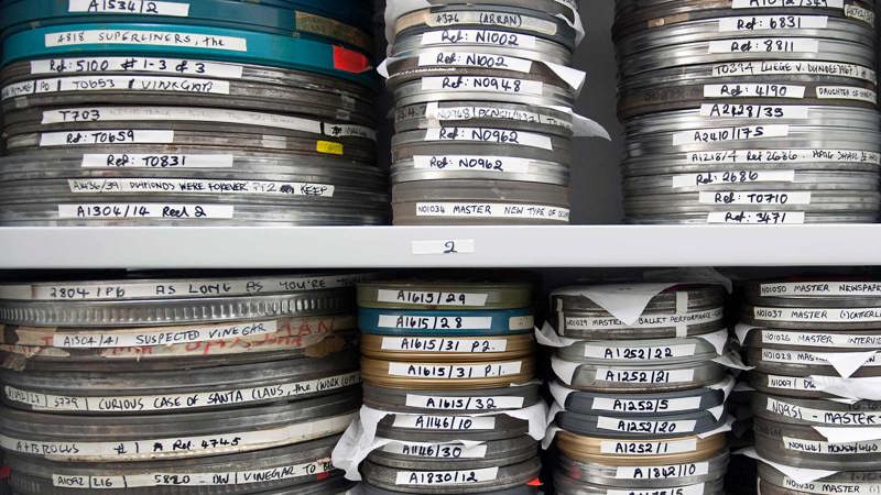 A grey shelf with stacks of film reels in cannisters arranged in large piles.