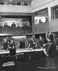 A WAAF ops room. There are women standing around a table on phones.