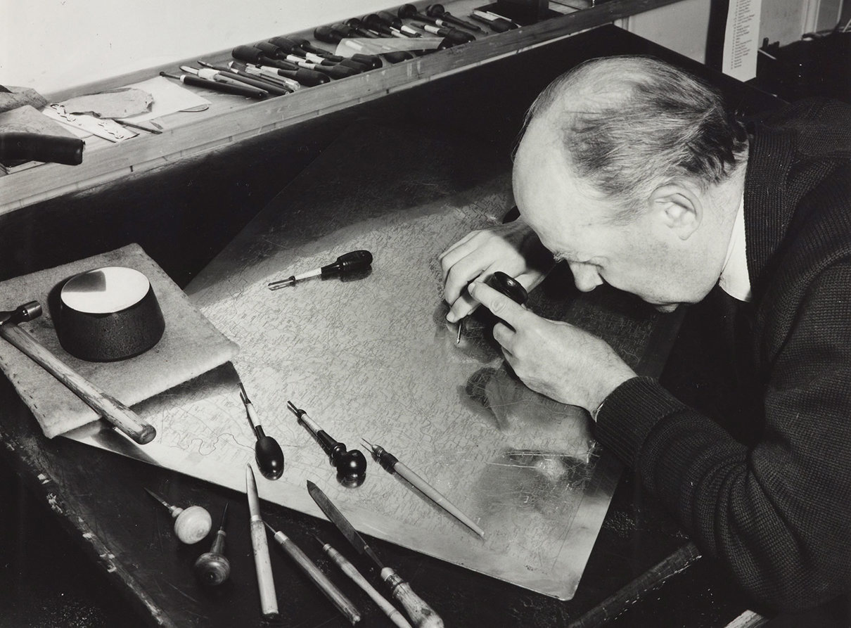 A black and white photo of a man engraving copper plate. 
