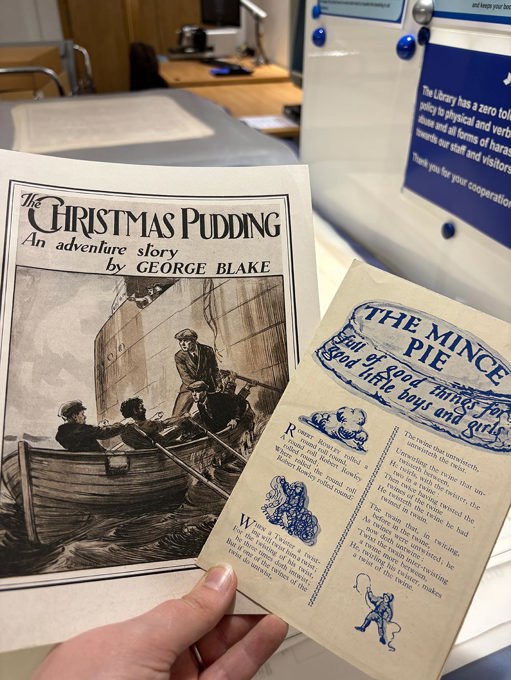 Two vintage holiday-themed printed pieces held by a hand. One is titled The Christmas Pudding: An adventure story by George Blake, showing people in a boat near a ship. The other, The Mince Pie, features blue ink illustrations and festive text.