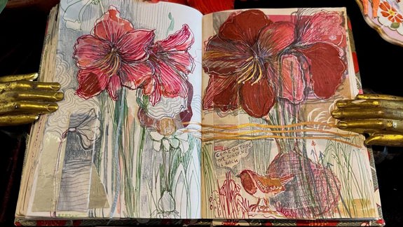 A sketchbook opened to a page with sketches of red flowers in a vase.