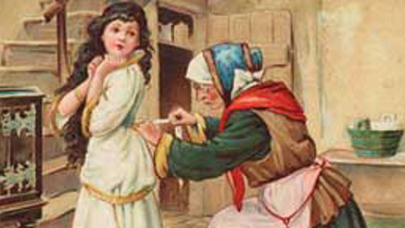 An older person in traditional clothing adjusts the back of a young woman’s white and gold dress inside a rustic wooden home.