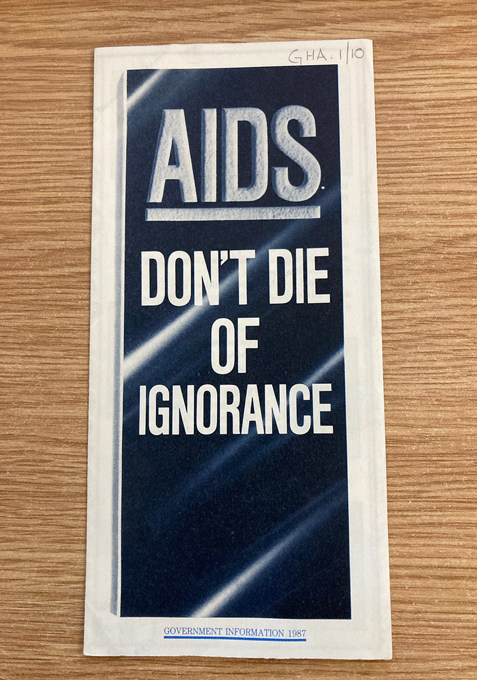 Pamphlet with a bold title 'AIDS' at the top. Below it, a message reads 'DON'T DIE OF IGNORANCE' in white capital letters on a dark blue background. At the bottom, it states 'GOVERNMENT INFORMATION 1987.'