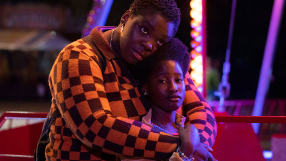 A mother hugs her daughter with fairground lights in the background.