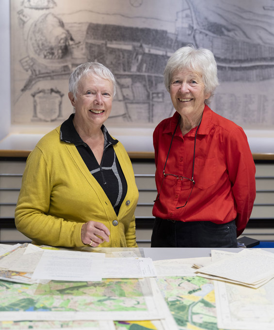 Two women standing behind a table with maps on it.