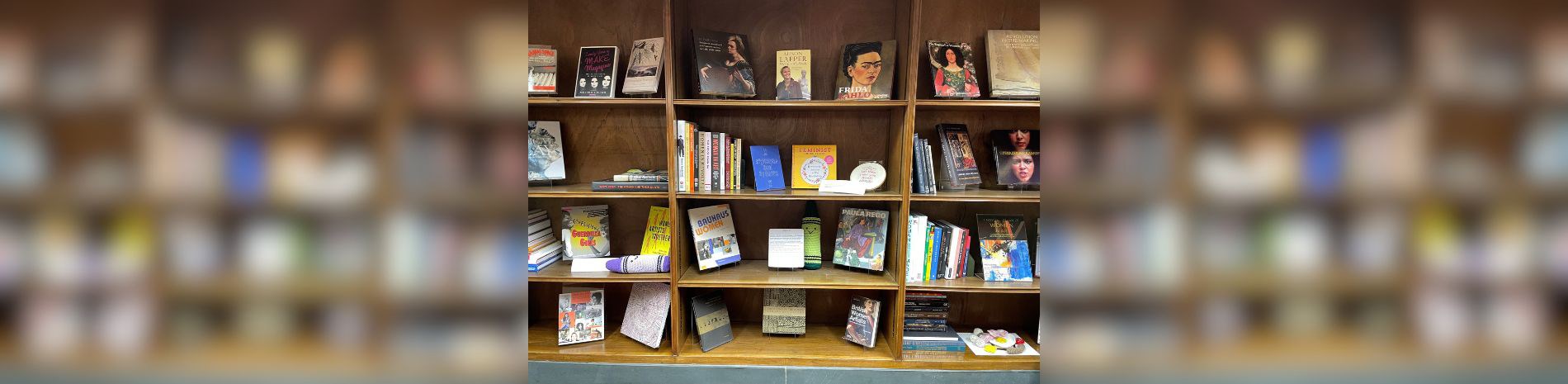 A photo of the Open Shelves display showing several bookshelves full of books about women artists and some crocheted crayons with smiley faces.